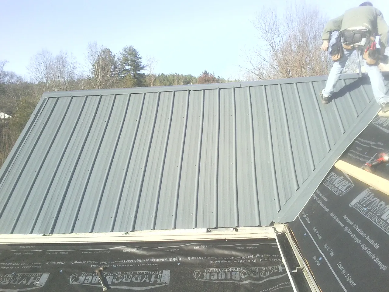 Crew installing dark green standing seam panels over synthetic underlayment in Dingmans Ferry