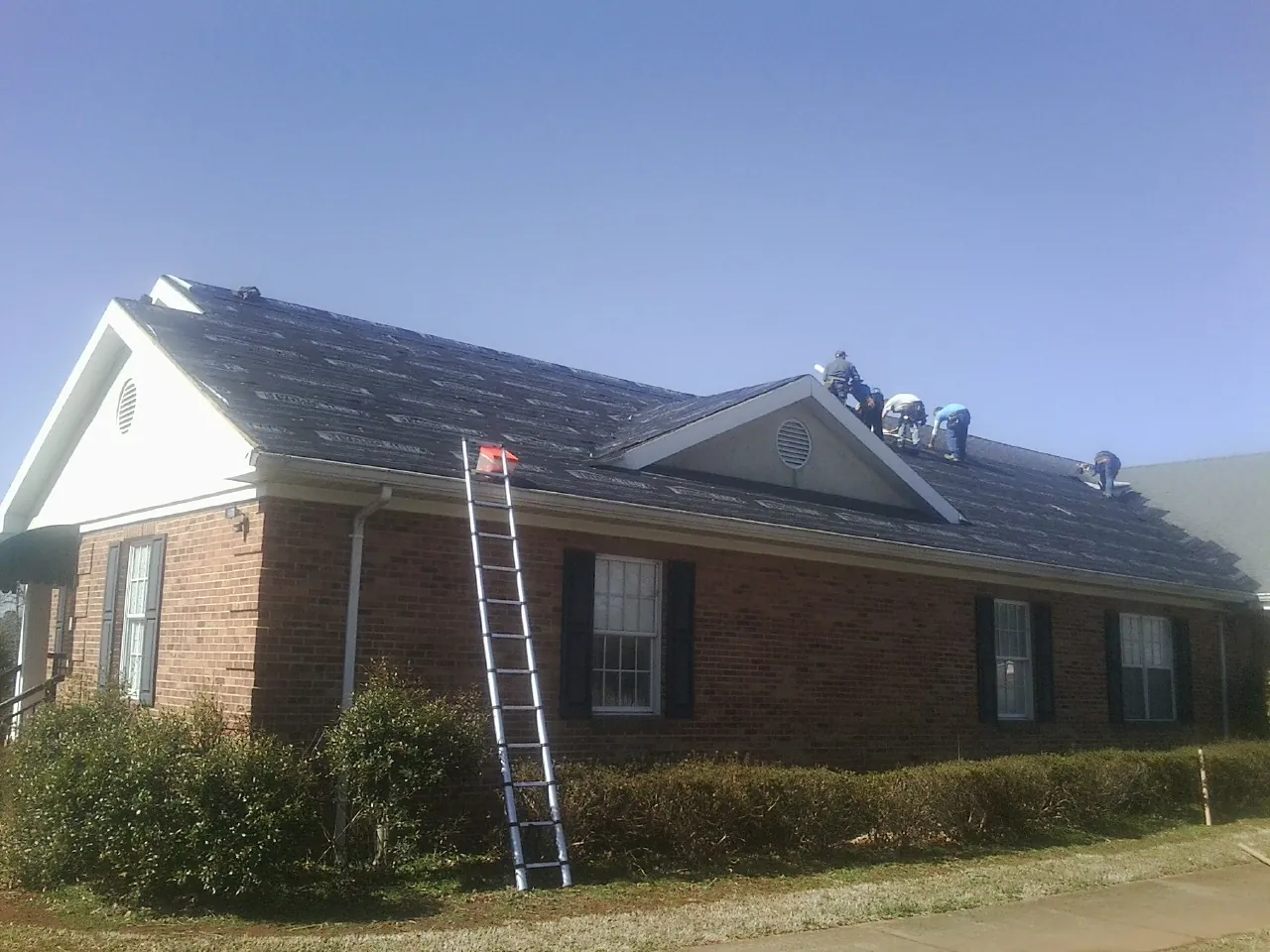 Crew tearing shingles off a brick ranch roof with a ladder set — Metal Roof Repair work by our crew in Dingmans Ferry