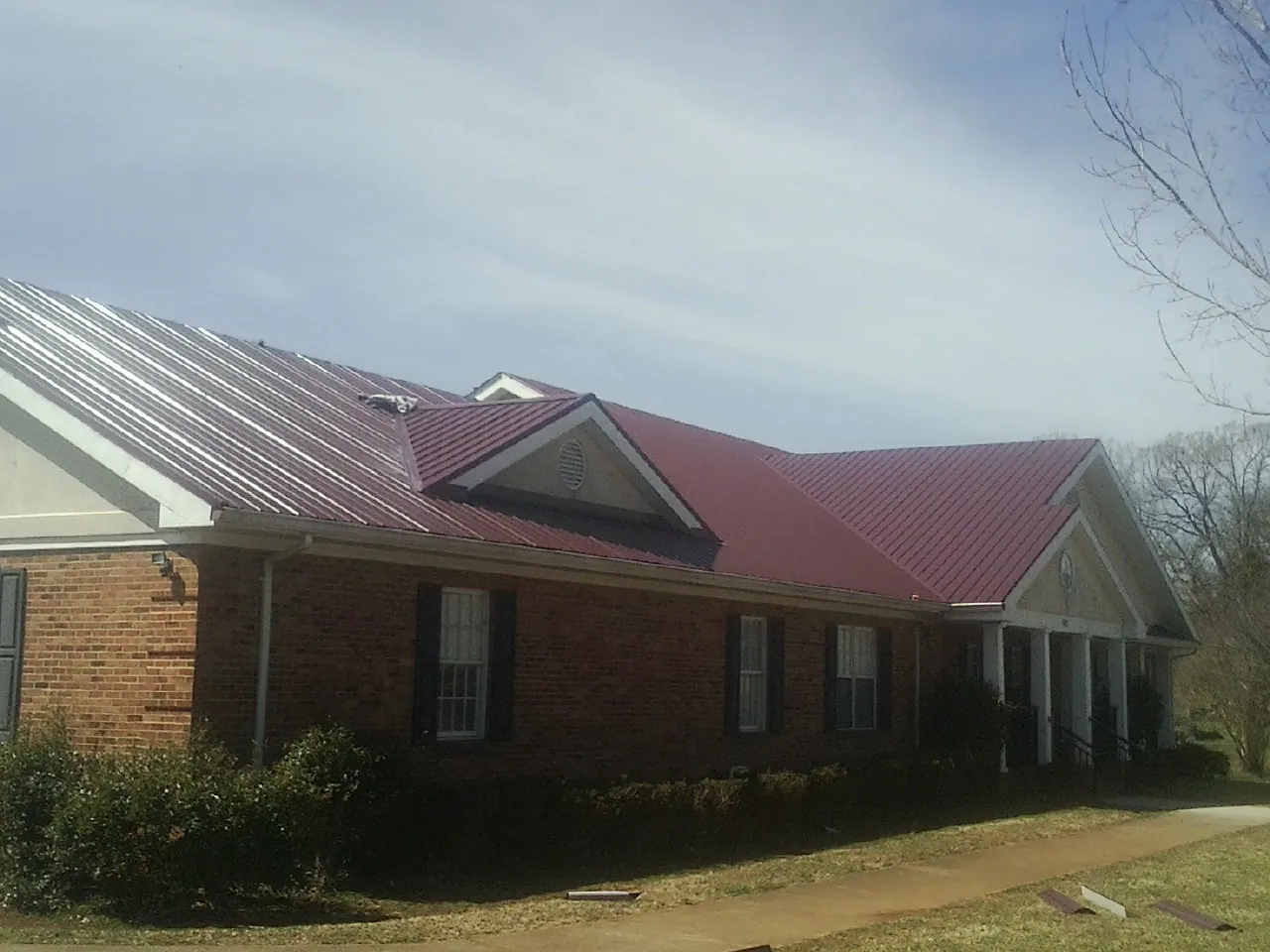 Red metal roof with gabled entries on a long brick building, from a Hail Damage Roof Repair job in Dingmans Ferry