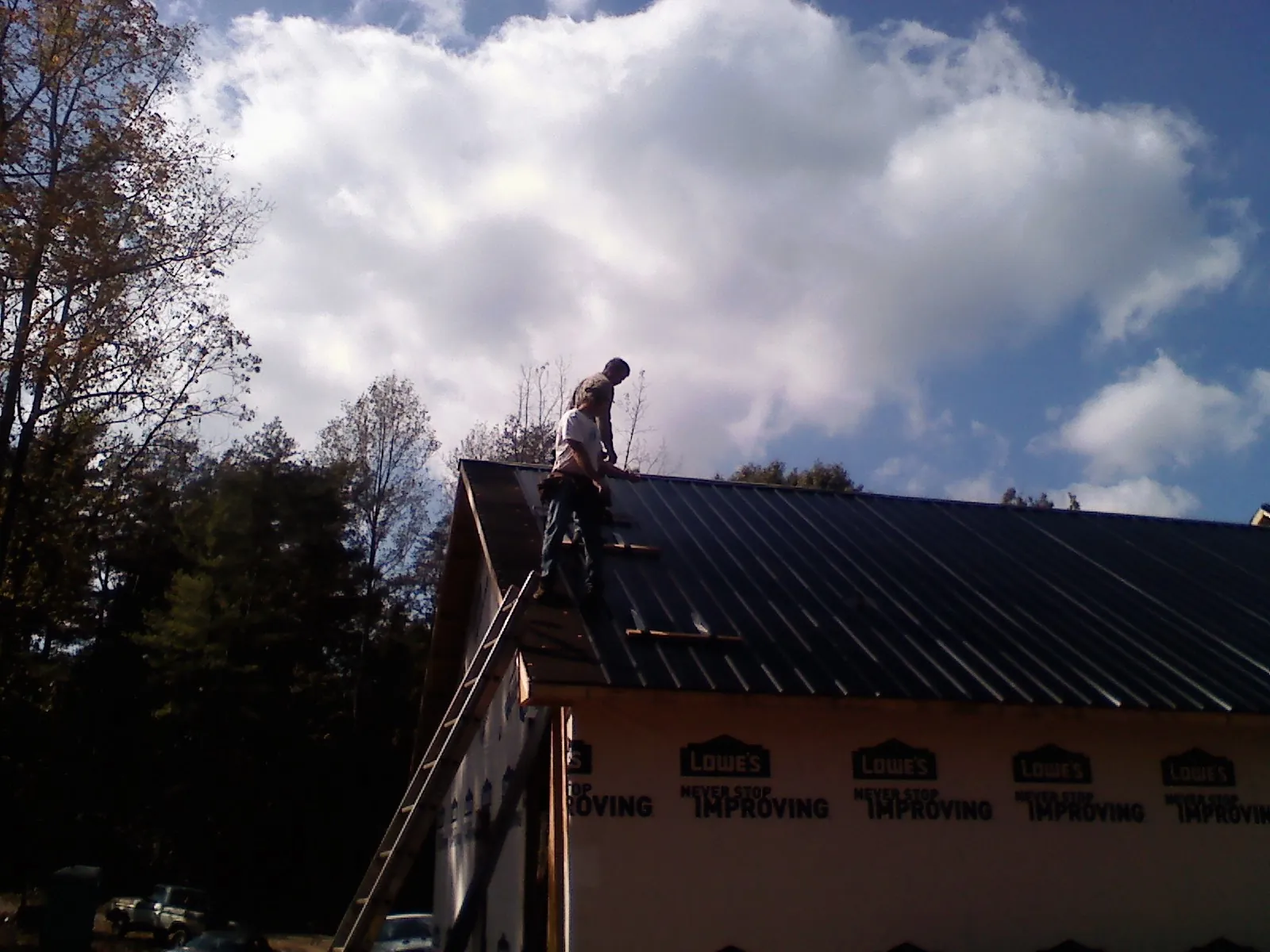 Roofer fastening dark metal panels high against a cloudy sky, from a Roof Inspection job in Dingmans Ferry