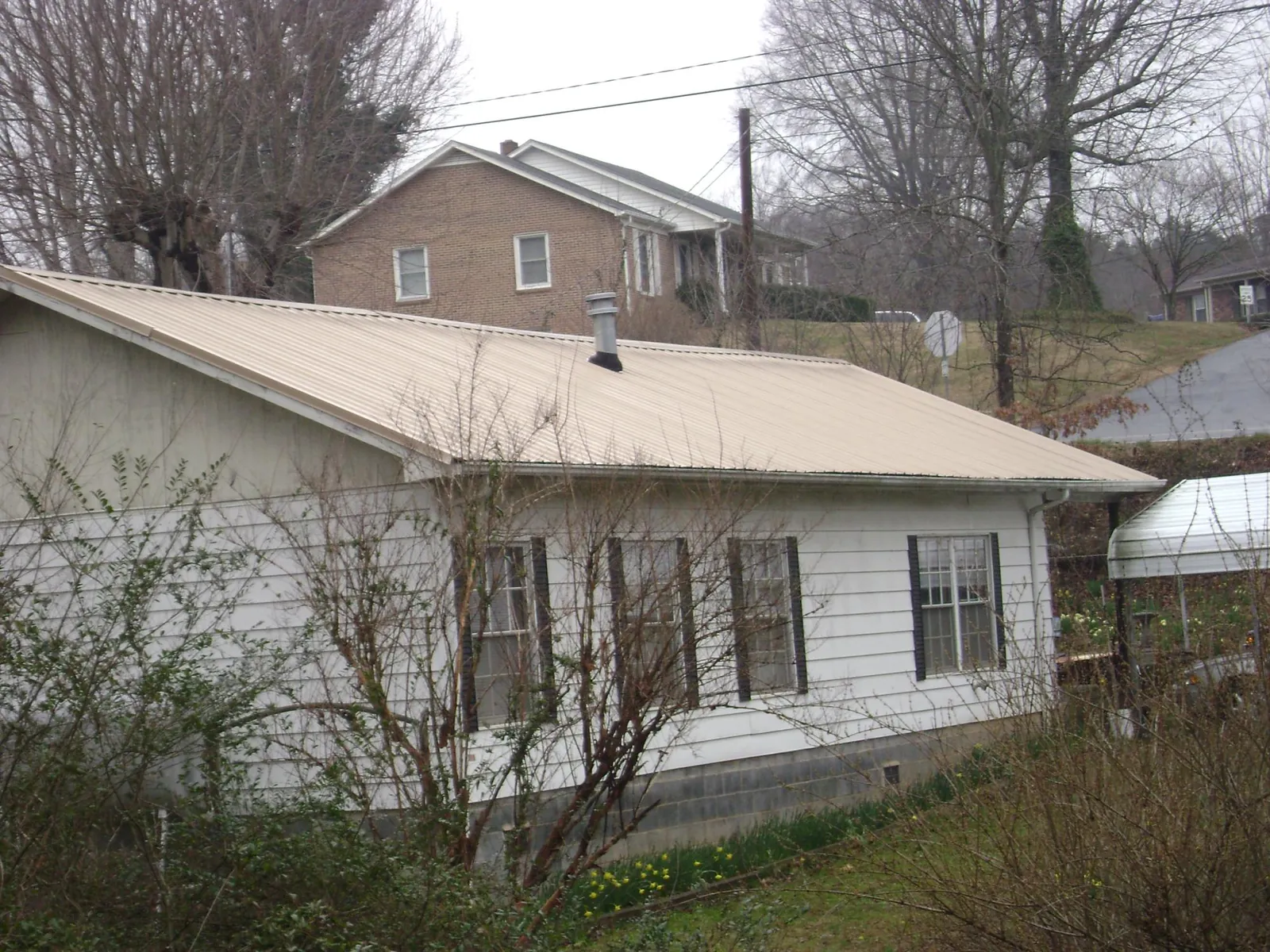 Tan metal roof on a white sided house set into a hillside — Commercial Roofing by Roofing Brothers in Dingmans Ferry